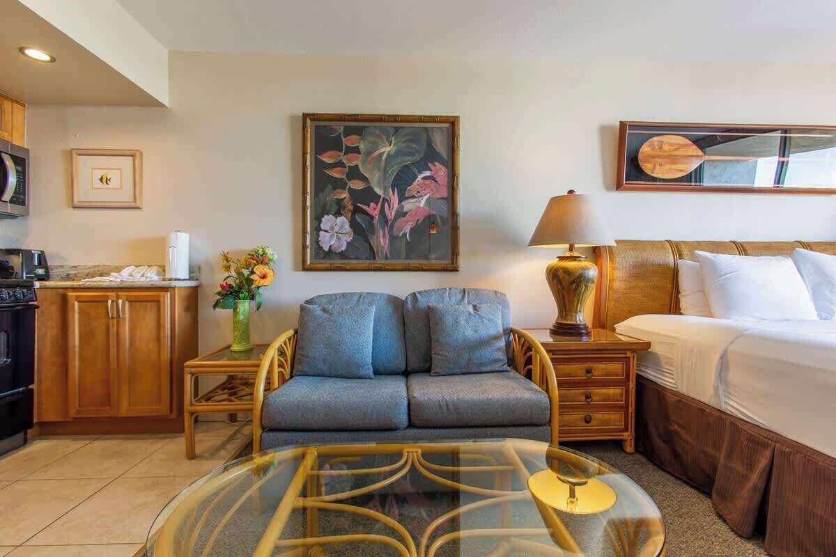 Ein Hotelzimmer mit einer Couch, einem Bett, einem Tisch, einer Lampe, einem Gemälde, einer Mikrowelle und einem Schrank.