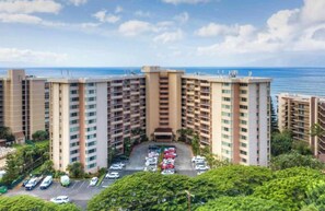 A multi-story hotel with a central courtyard parking area, surrounded by greenery and overlooking a body of water. - 8th floor resort studio, AC, stunning ocean views, walkable area (Lahaina)