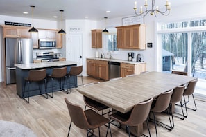 A modern kitchen with wooden cabinets, a central island, bar stools, and a large dining table.
