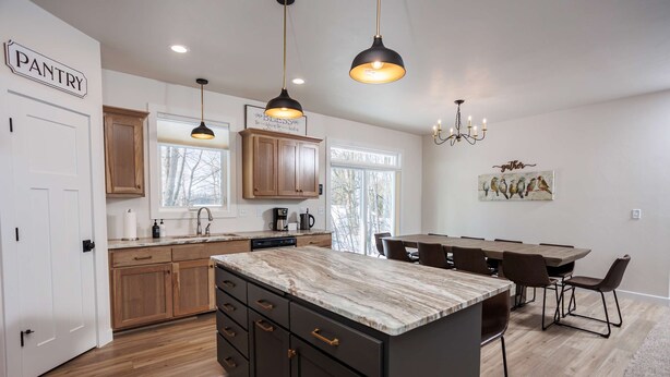 Una cocina moderna con armarios de madera, una isla de mármol, iluminación colgante y un comedor con sillas.