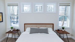 Un dormitorio con una cama grande, un cabecero y cuatro ventanas.