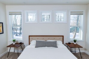 A bedroom with a large bed, a headboard, and four windows. - Downtown Sister Bay: 2022 New Construction home (Sister Bay)