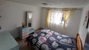 Ein Schlafzimmer mit einem Bett, einem Schminktisch, einem Spiegel und einem Fenster mit Vorhängen.