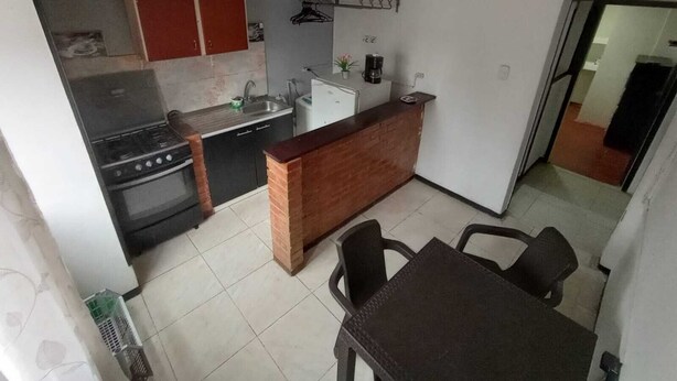 Eine kleine Küche mit Herd, Spüle und einem Kühlschrank. Ein Esstisch mit Stühlen und eine Arbeitsplatte aus Ziegelsteinen sind ebenfalls vorhanden.