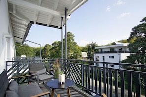 Un balcon avec une table et des chaises, un pot de fleurs et une vue sur un immeuble moderne et des arbres.