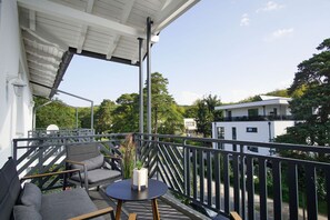 A balcony with a table and chairs, a potted plant, and a view of a modern building and trees.