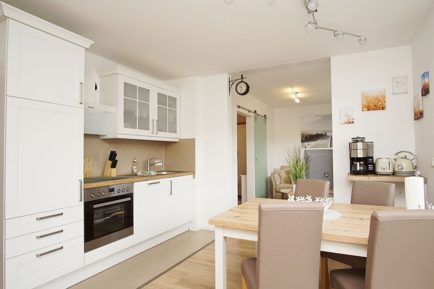 Una cucina moderna con mobili bianchi, un'area pranzo con tavolo e sedie in legno, e un piccolo angolo salotto con divano e tavolino.