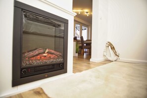 En modern öppen spis med en glasdörr, en matplats med ett bord och stolar samt en vit vägg med en repdekoration.