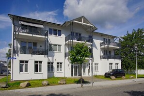 En flervåningsbyggnad med bostäder, balkonger och en bil parkerad framför, och en klar himmel.