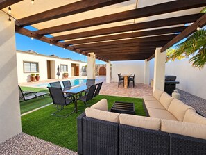 An outdoor patio with a pool, dining table, and lounge area.
