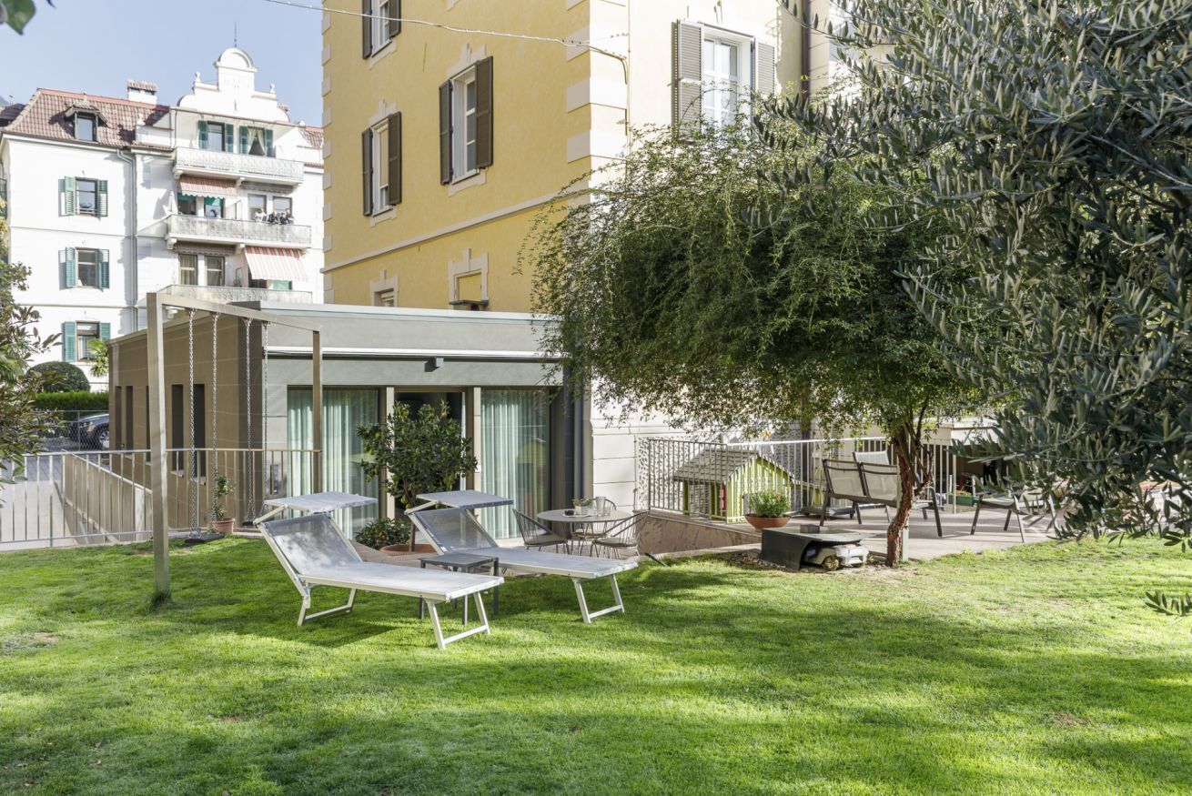 Un patio con mesas al aire libre, un pequeño jardín y un edificio con balcones.