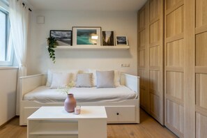 A modern bedroom with a white sofa, a bedside table with a vase and candle, and a shelf with framed pictures. - Casa Fiammetta near Bruneck (Brunico)