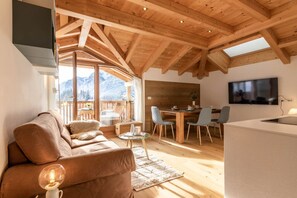 En hyggelig stue med træloft, sofa, spiseplads med stole og et TV ophængt på væggen.