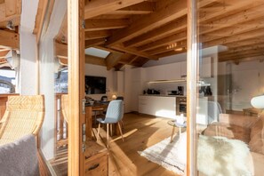 Une cuisine moderne avec des meubles blancs, un coin repas doté d’une table et de chaises en bois, et un espace salon confortable agrémenté d’un tapis et de coussins.