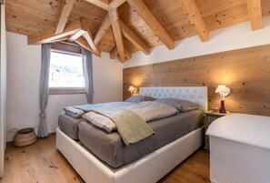Une chambre avec un grand lit, des poutres apparentes en bois au plafond, une fenêtre avec des rideaux et des lampes de chevet.