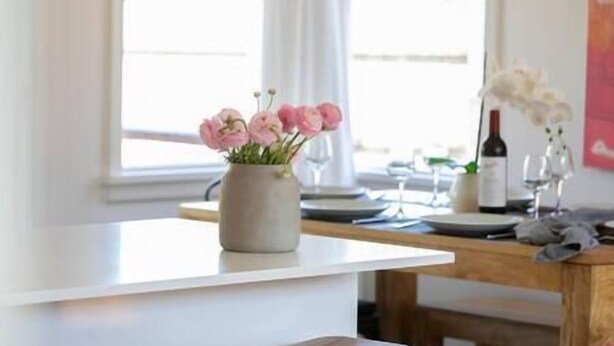 Una zona de dinar amb una taula ben a punt per a dues persones, un vas amb flors roses i una ampolla de vi sobre la taula.