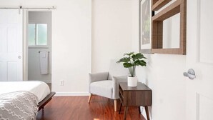 Une chambre à coucher avec un lit, une chaise, une petite table avec une plante, un miroir et une porte.