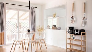 Une cuisine moderne avec un coin repas, comprenant une table et des chaises en bois, une machine à café et une étagère contenant des ustensiles de cuisine.
