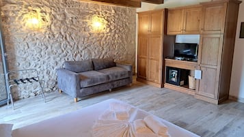 A room with a stone wall, wooden ceiling beams, a sofa, a TV cabinet, and a bed with towels.