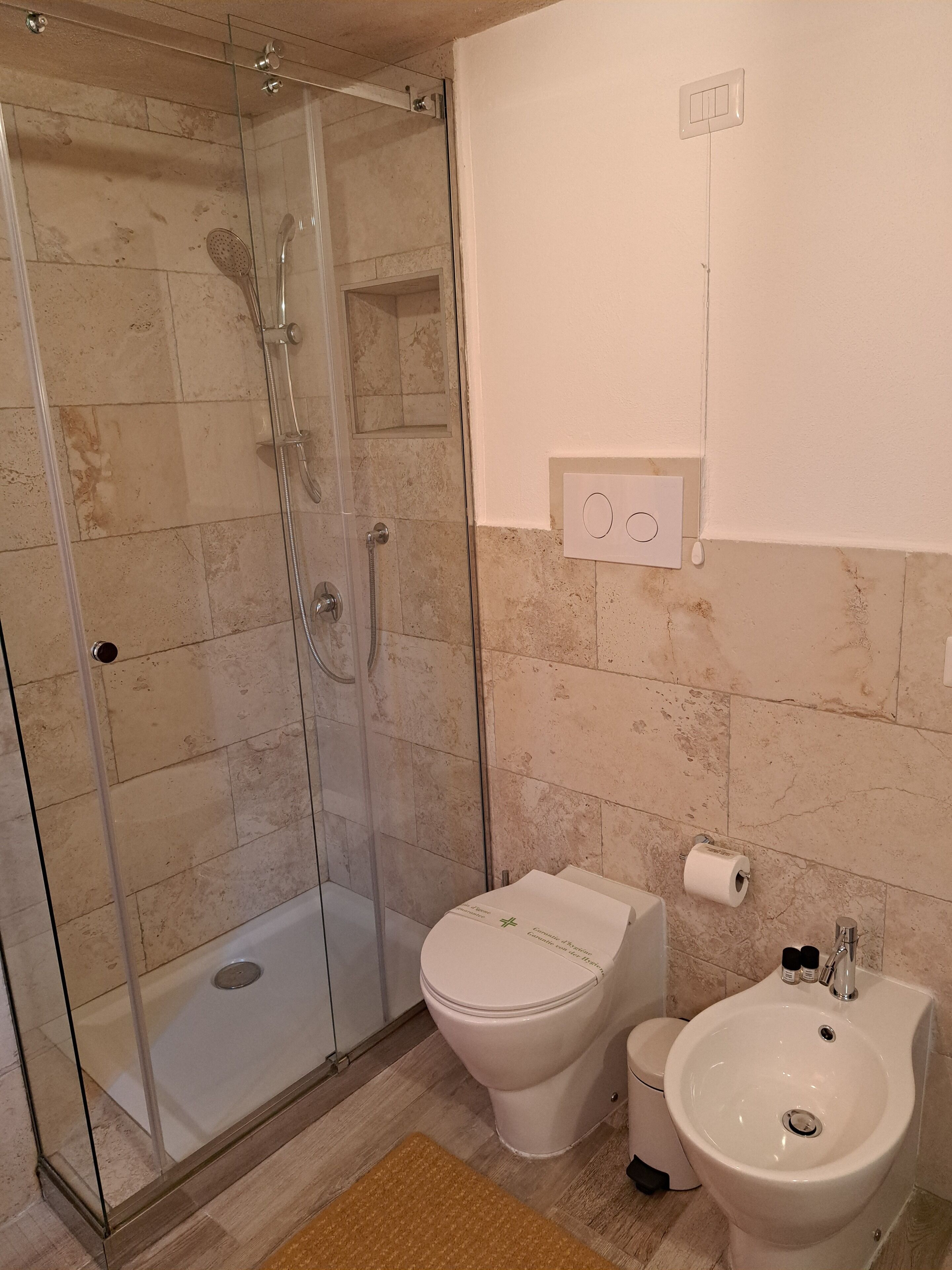 Un baño con ducha de mampara de vidrio, inodoro y lavamanos.