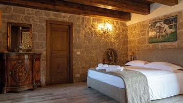 A bedroom with a stone wall, wooden ceiling, a bed with white linens, a wooden dresser, and a painting of horses.