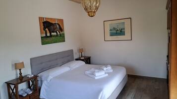 A bedroom with a large bed, two bedside tables, a chandelier, and two framed pictures on the wall.