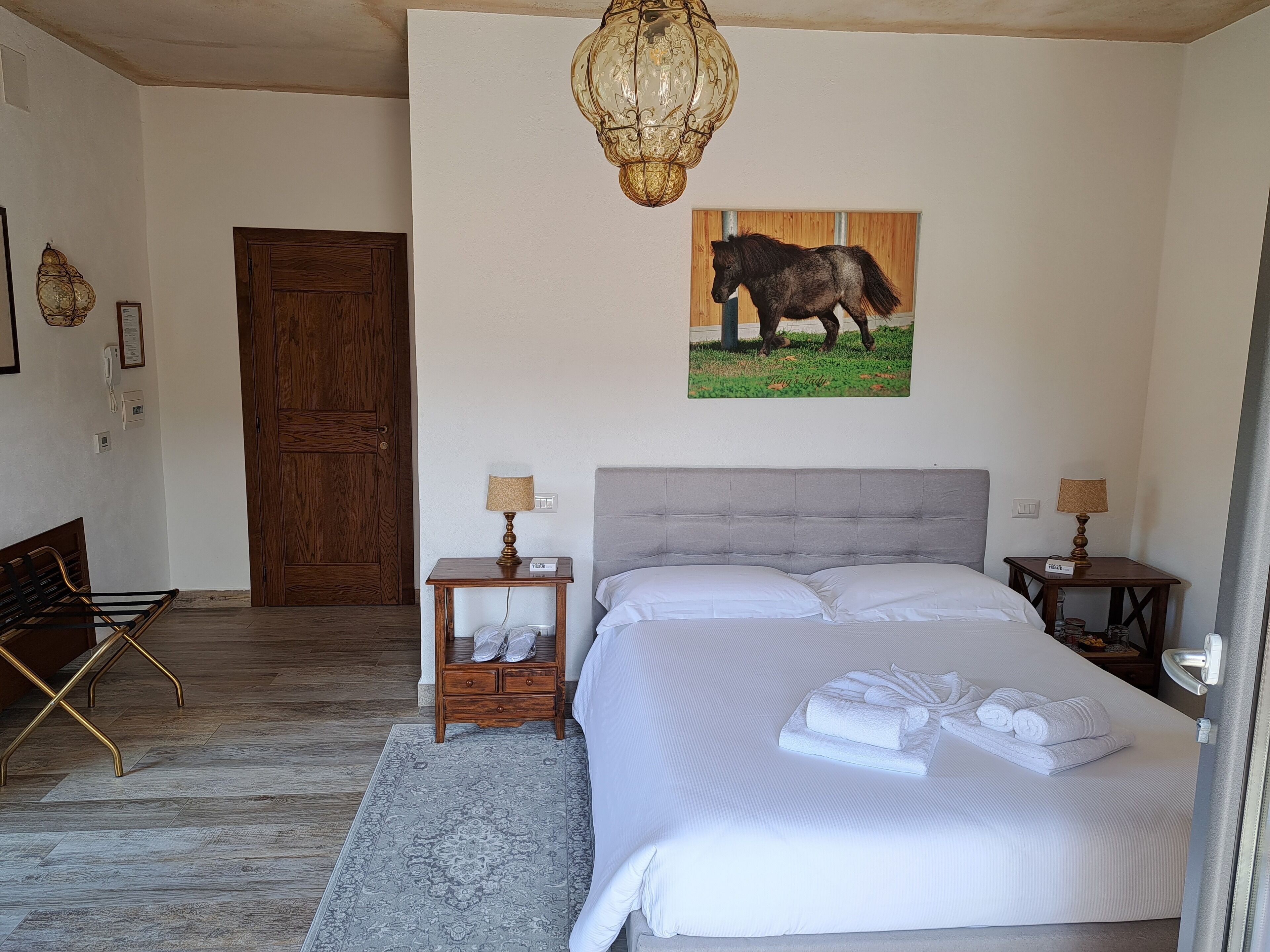 A bedroom with a bed, two bedside tables, a wooden door, a bench, and a chandelier.