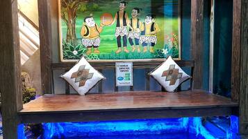 A wooden bench with two decorative pillows, a framed illustration of a family, and a sign with text in a foreign language.