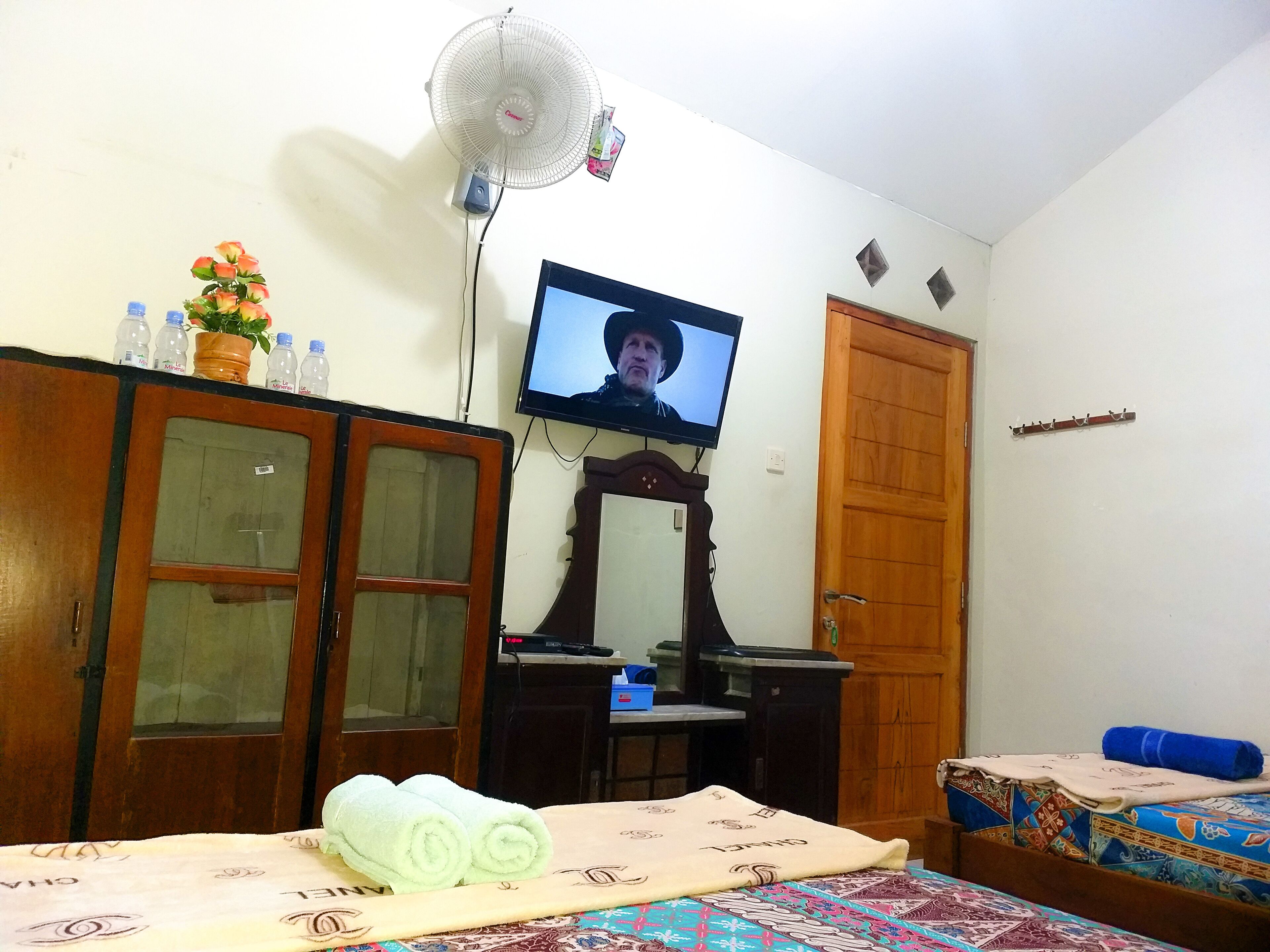 A room with a bed, a desk, a television, a wardrobe, and a wall-mounted fan.