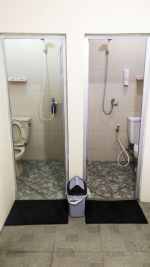 A public restroom with two stalls, each equipped with a toilet, a shower, and a hand dryer. There is a trash bin in the center. - Ngampilan Backpacker Hostel (Yogyakarta)
