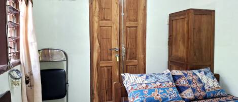 A bedroom with a wooden wardrobe, a metal shelf, a bed with patterned bedding, and a curtain.