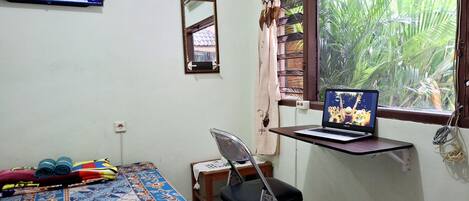 Una stanza con un letto, una scrivania con un portatile, una TV a parete e una finestra con tende.