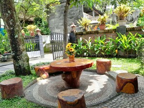 A round wooden table with a vase of yellow flowers, surrounded by four wooden stools. - Ngampilan Backpacker Hostel (Yogyakarta)