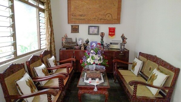 A traditional room with wooden furniture, a central table with a vase, and a window with curtains. - Ngampilan Backpacker Hostel (Yogyakarta)