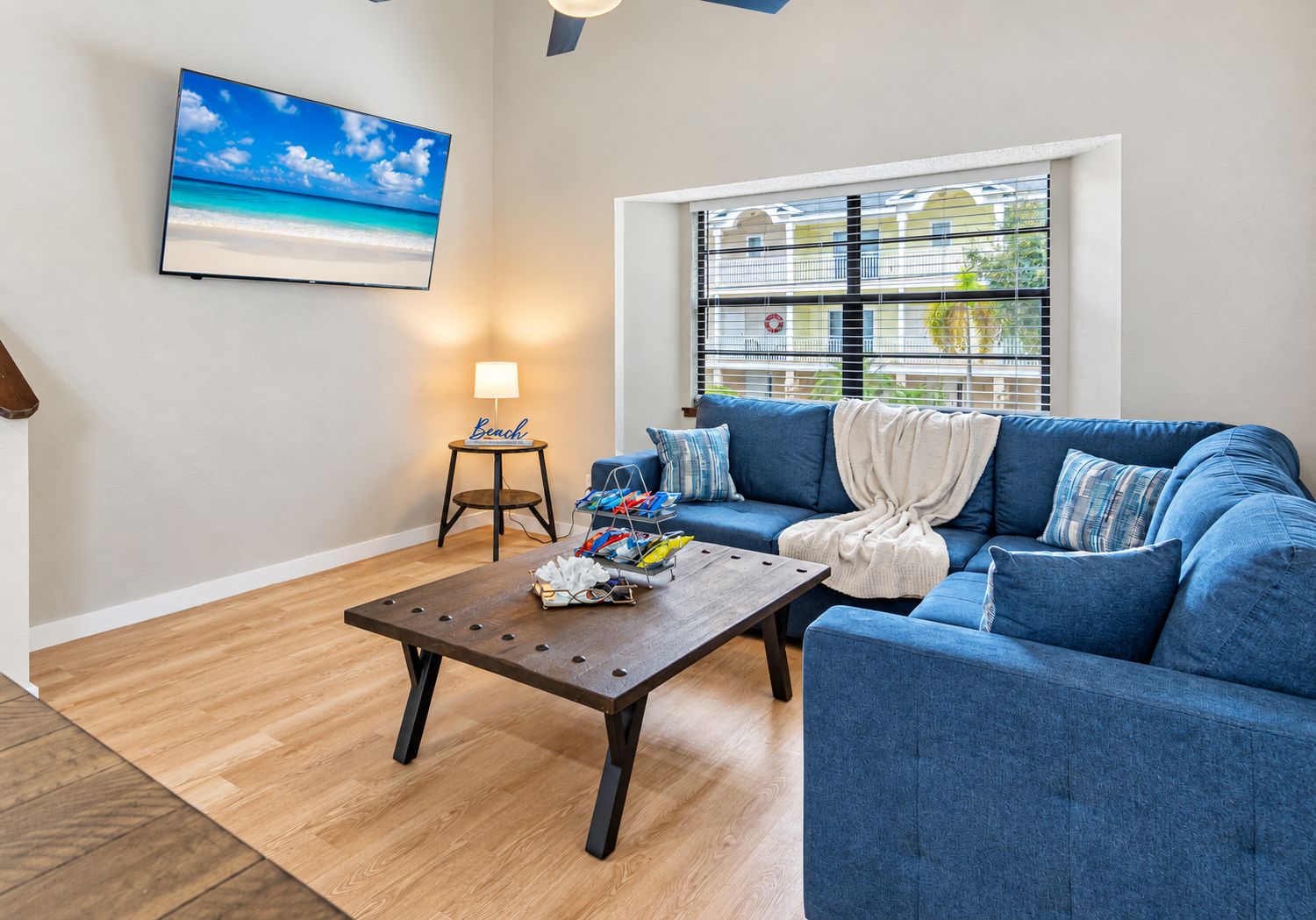 Ein Wohnzimmer mit blauem Sofa, Couchtisch, Lampe und Fernseher im Strandhausstil.