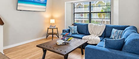 Ein Wohnzimmer mit blauem Sofa, Couchtisch, Lampe und Fernseher im Strandhausstil.