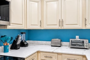 A kitchen with white cabinets, a blue wall, a toaster, a blender, and various utensils.