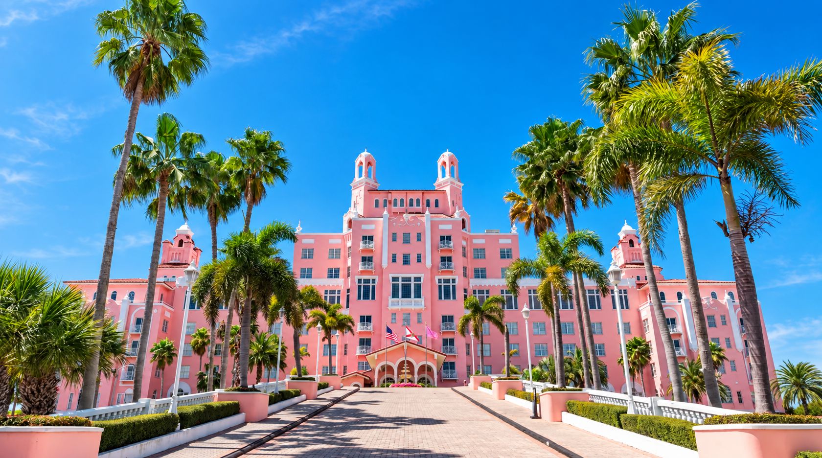 A pink building with a central entrance, surrounded by palm trees.