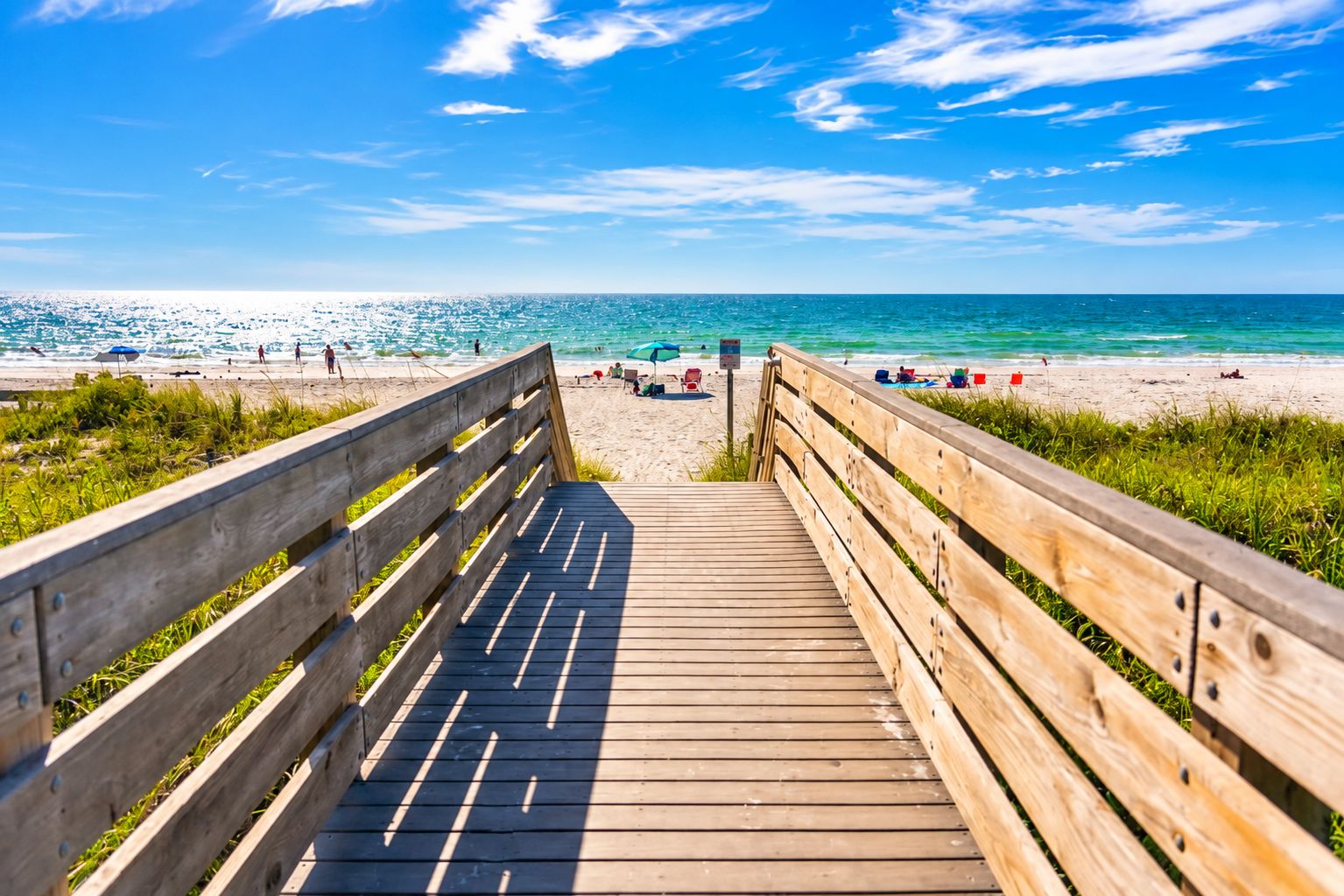 A wooden boardwalk leading to a beach with clear skies.