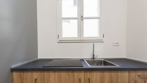 A kitchen with a black induction cooktop, a stainless steel sink, wooden cabinets, and a window above the sink. - Firenze Duomo Suite apartment by Mmega (Firenze)