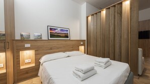 A modern hotel room with a wooden headboard, a bed with white linens, and a framed landscape picture on the wall. - Firenze Duomo Suite apartment by Mmega (Firenze)