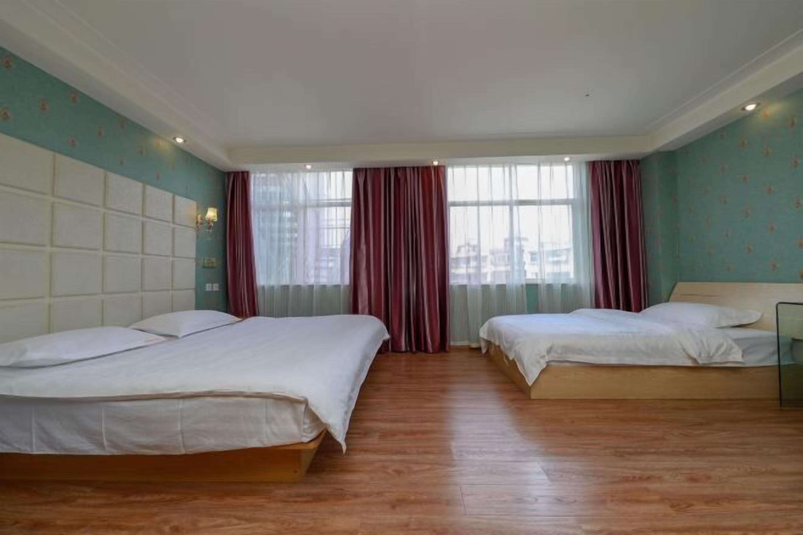 Hotellihuone, jossa on kaksi sänkyä, suuri ikkuna, jossa on verhot, ja puulattia.