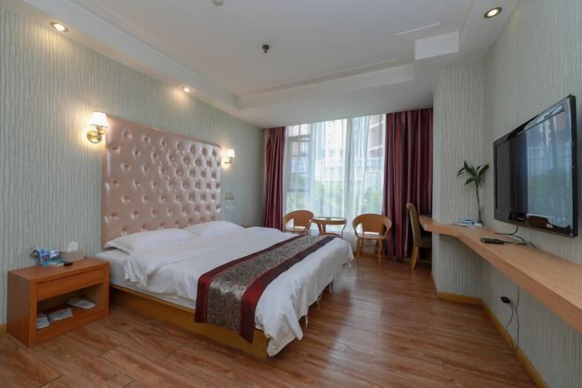 A hotel room with a large bed, a TV, a desk, and a chair.
