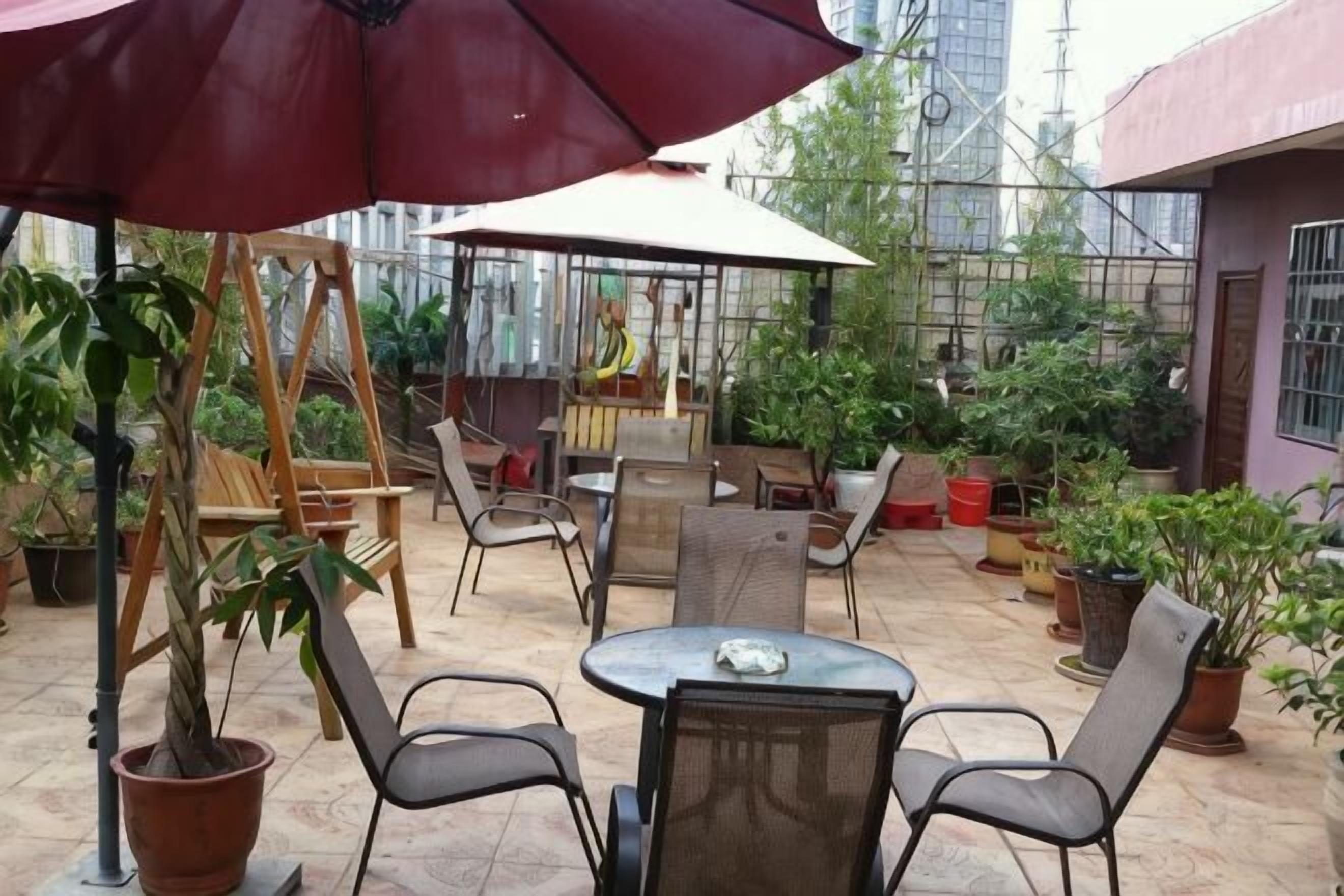 An outdoor patio with tables, chairs, and umbrellas, surrounded by potted plants.