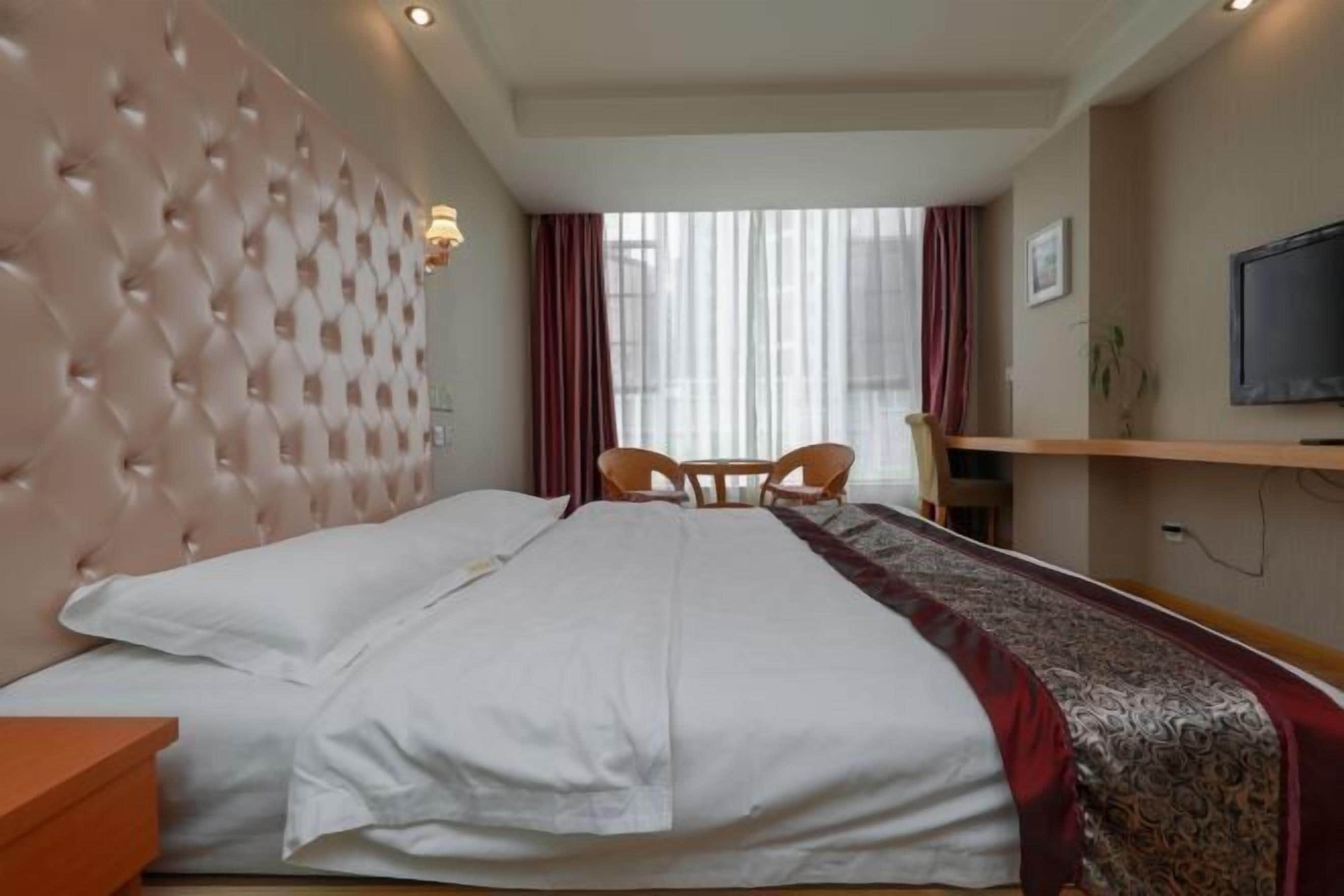A hotel room with a large bed, a TV, a desk, and a chair.
