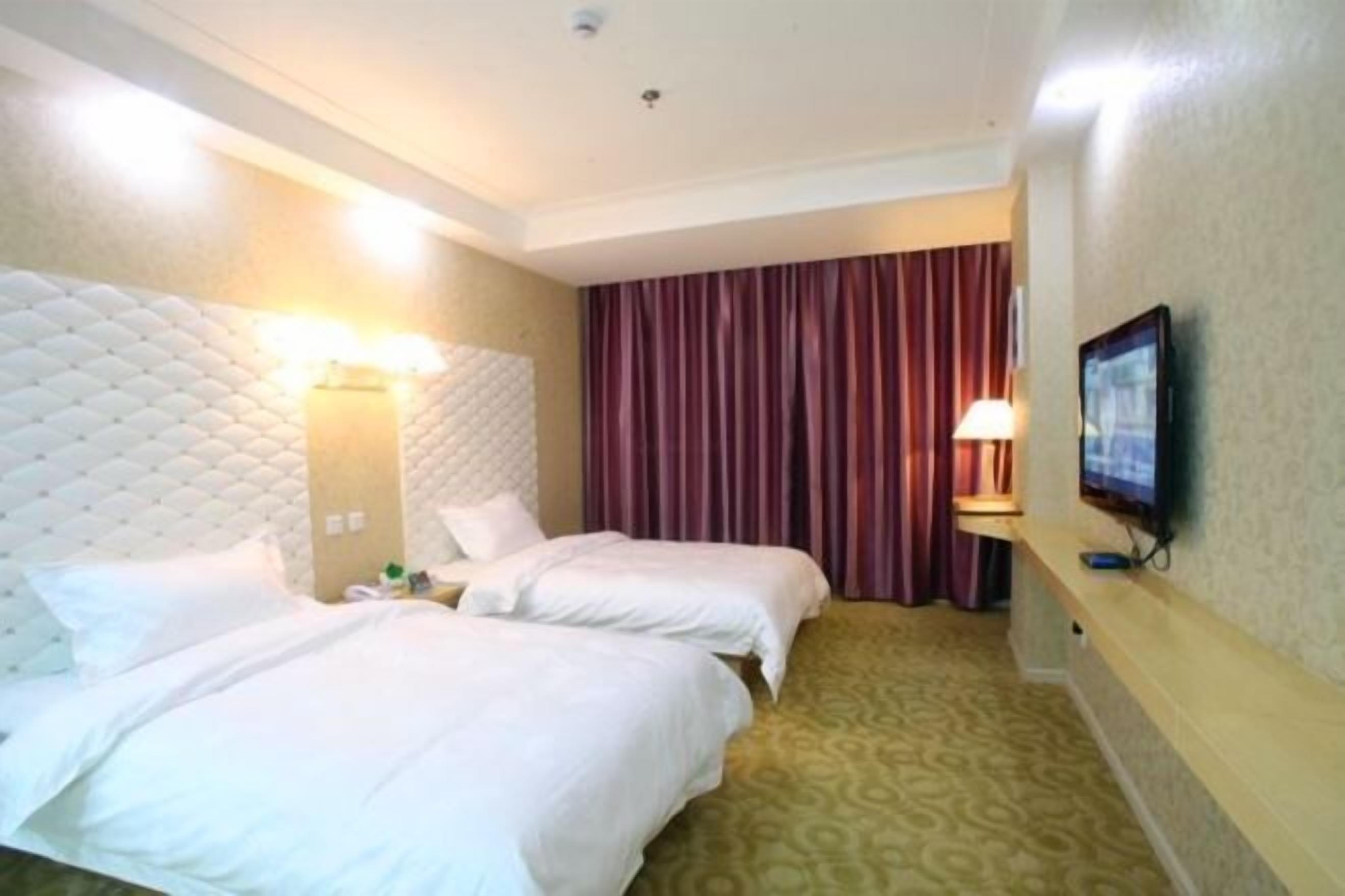 A hotel room with two beds, a television, and a patterned carpet.