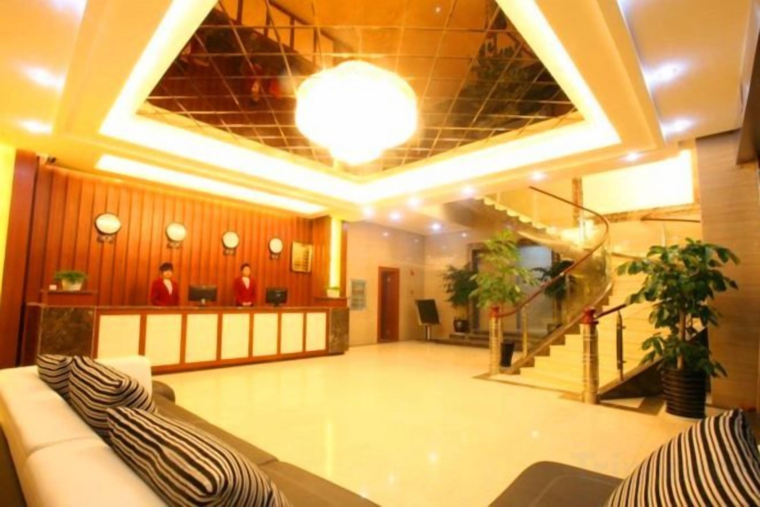 A hotel lobby with a reception desk, seating area, staircase, and potted plants.