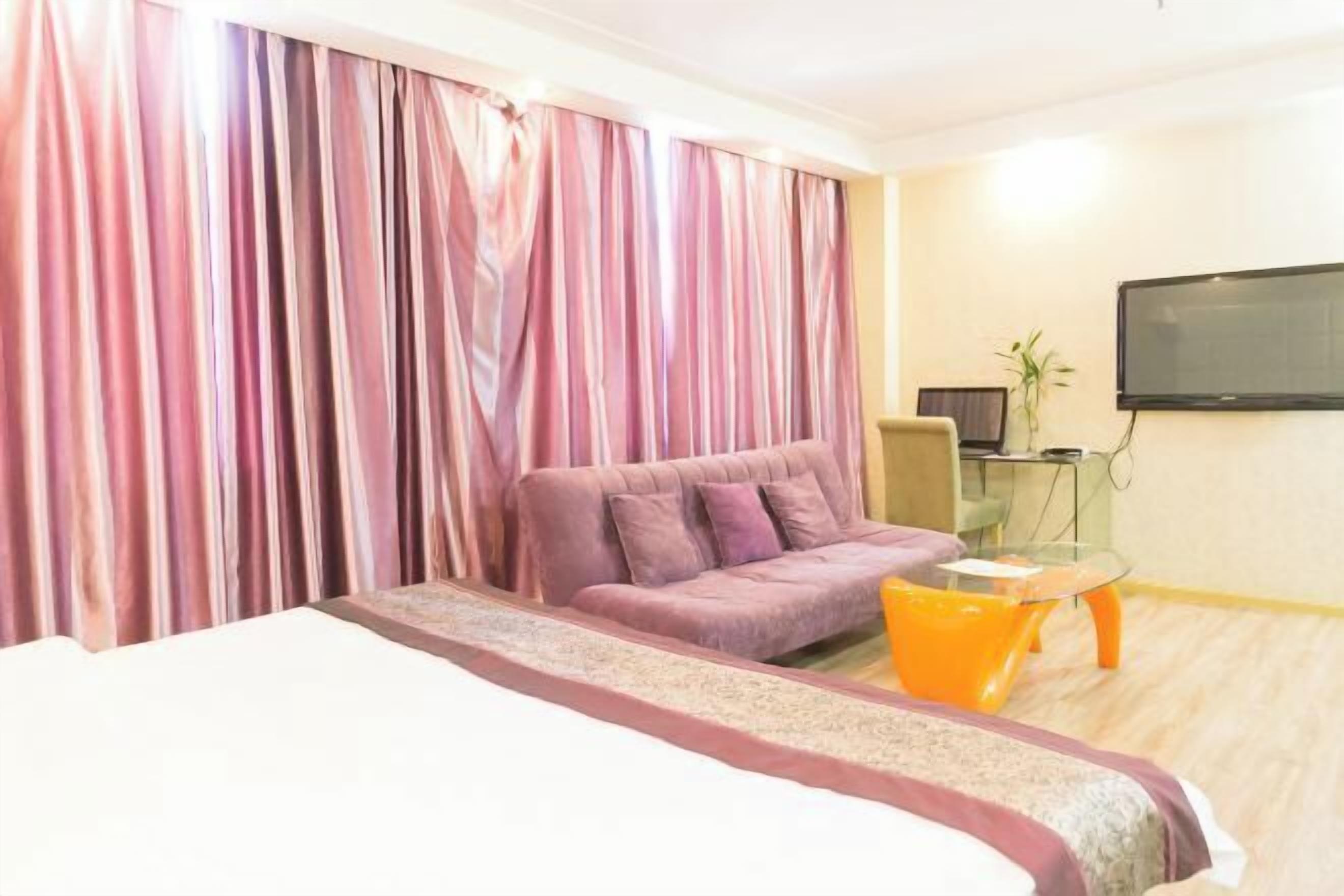 A hotel room with a bed, a sofa, a small table, a TV, and curtains.