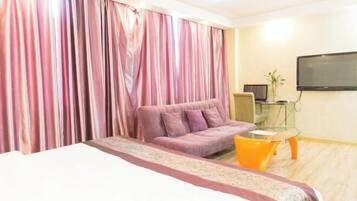 A hotel room with a bed, a sofa, a small table, a TV, and curtains.