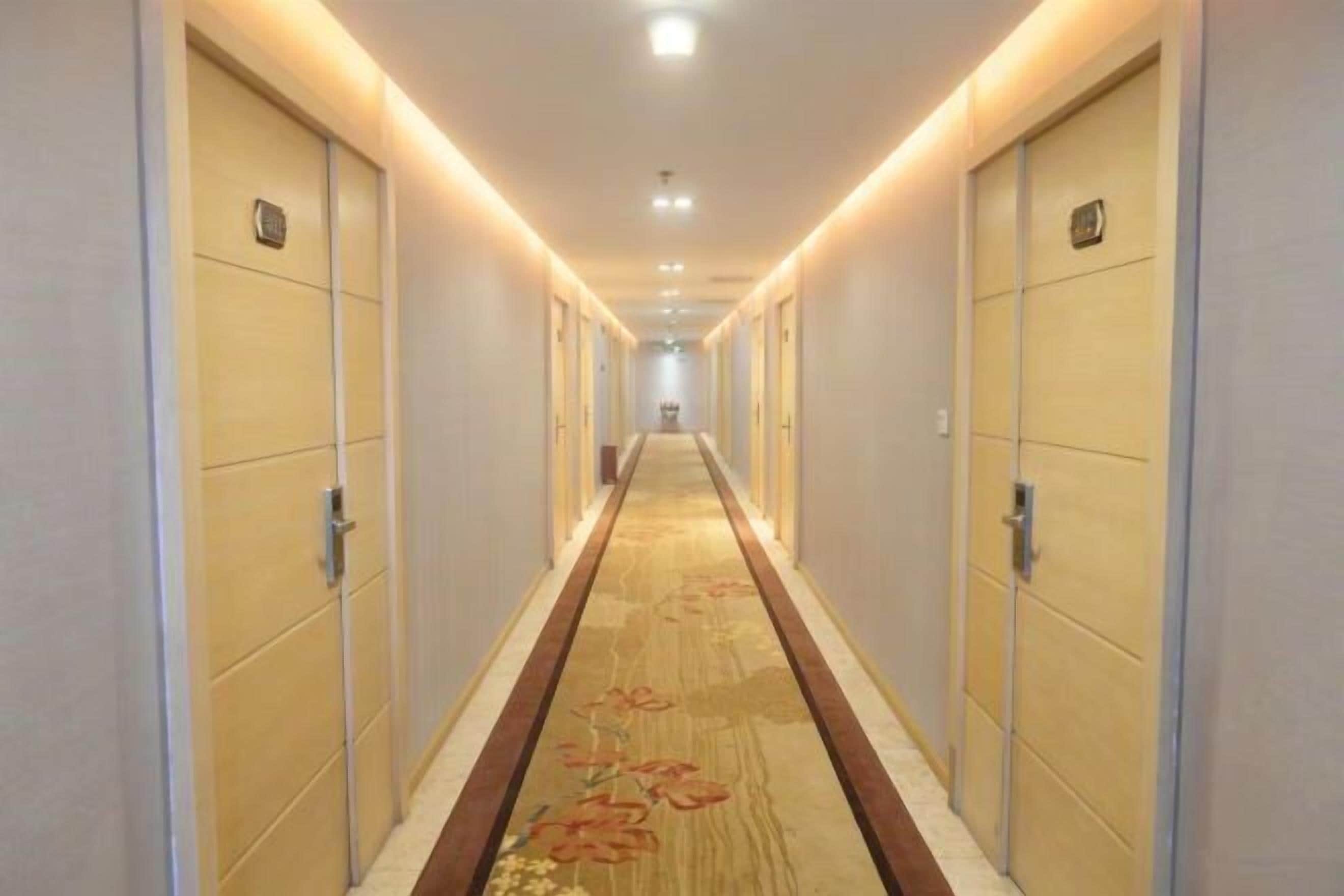Un pasillo de hotel con puertas a ambos lados, una alfombra de estampado floral e iluminación en el techo.